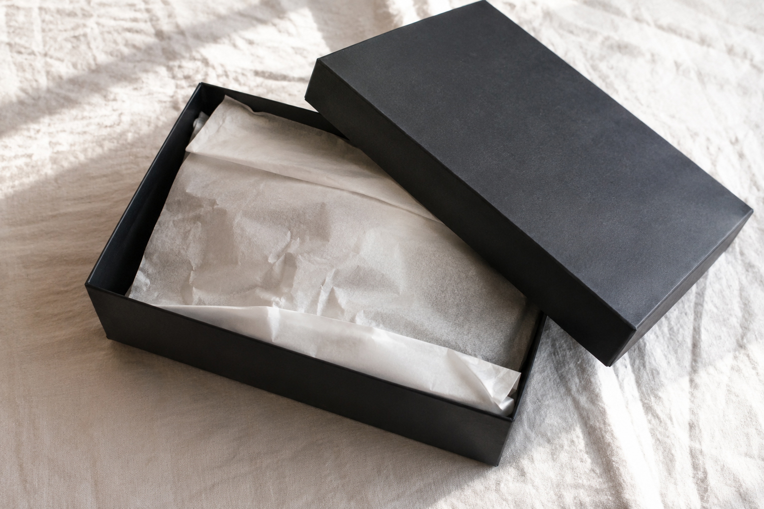 Black luxury box with lid open showing white crinkle paper covering an item