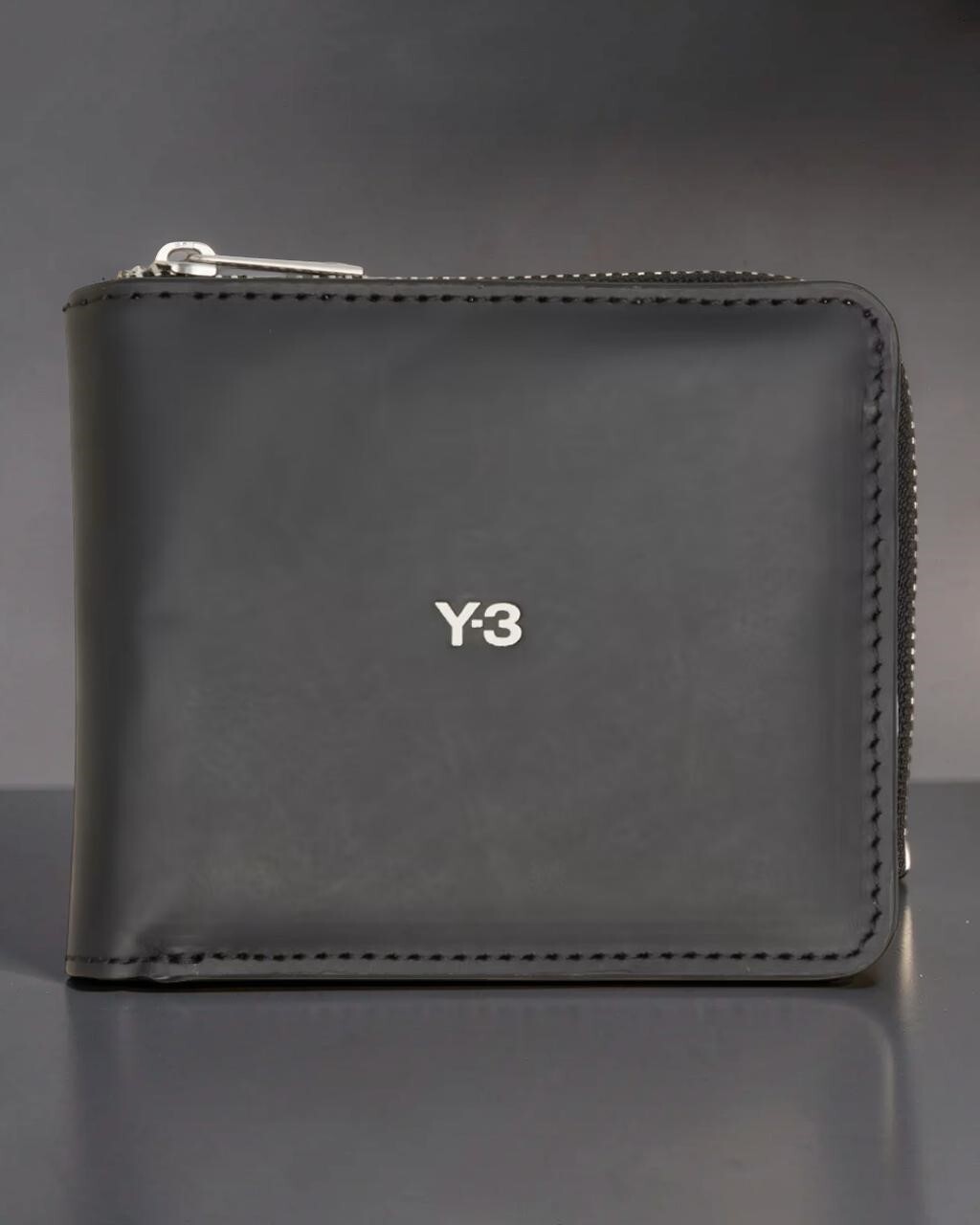 Y-3 Black Bifold Leather Wallet with white Y-3 logo & zip front view standing on grey surface